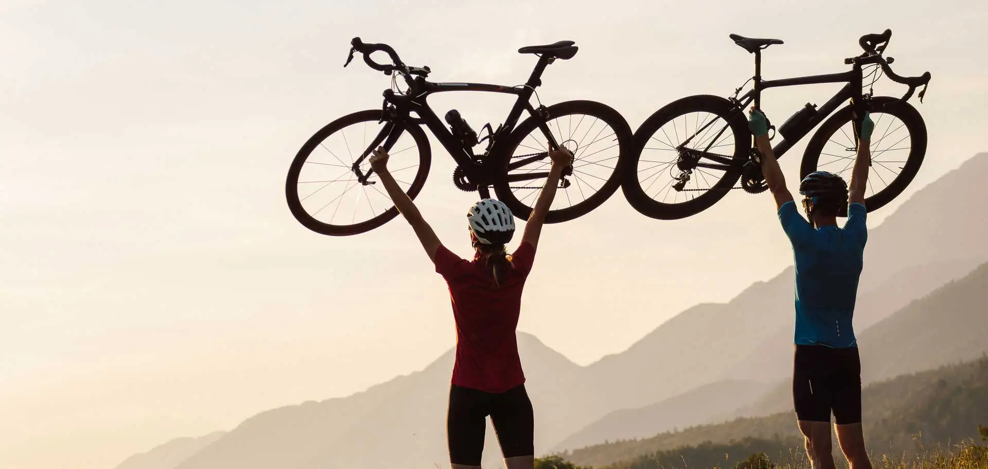Man and woman couple on a self guided road cycling tour celebrating with their bikes lifted above their heads and enjoying the scenery.